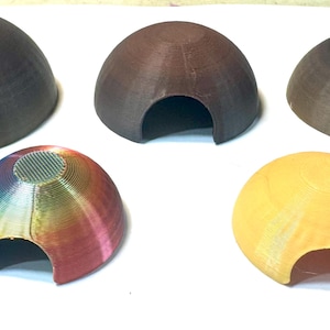 May include: Five dome-shaped structures with arched openings at the base. Three are dark brown, one is a multi-colored gradient featuring red, yellow, green, and blue, and one is a solid light yellow. Each piece has a visible layered texture.