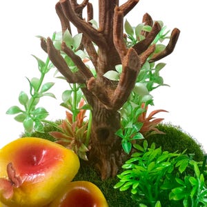 May include: A miniature forest scene featuring a brown tree trunk, green foliage, and three yellow mushrooms with red tops.