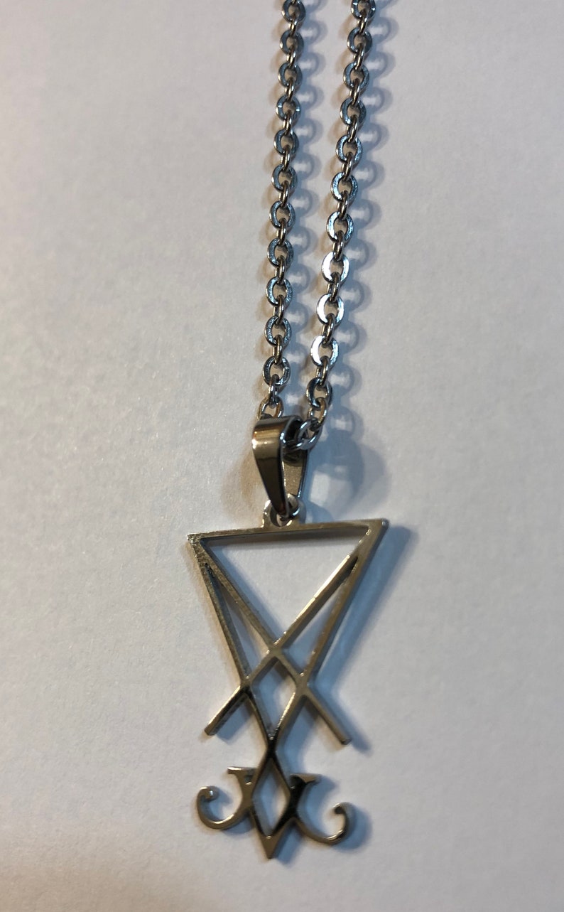 Puede incluir: Un collar de cadena de plata con un colgante de plata que presenta un s&iacute;mbolo de pentagrama con una 'V' estilizada en la parte inferior.