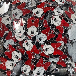 May include: A large pile of silver charms featuring a cartoon character with red bows and black eyes. The charms are all identical and are arranged in a random pattern.