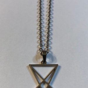 Puede incluir: Un collar de cadena de plata con un colgante de plata con un s&iacute;mbolo de pentagrama.