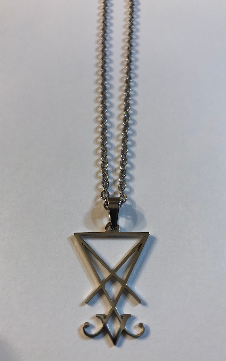 Puede incluir: Un collar de cadena de plata con un colgante de plata con un s&iacute;mbolo de pentagrama.