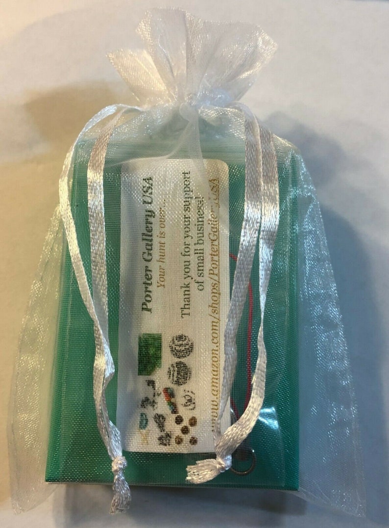 Puede incluir: Una peque&ntilde;a caja verde con una etiqueta blanca que dice "Porter Gallery USA" y "Your hunt is out." La etiqueta tambi&eacute;n incluye un mensaje de agradecimiento por el apoyo a las peque&ntilde;as empresas y una direcci&oacute;n de sitio web. La caja est&aacute; en una bolsa de organza blanca con lazos de cinta blanca.