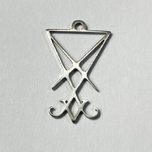Puede incluir: Un colgante de plata con un pentagrama invertido estilizado con una cruz en su interior. El colgante tiene un bucle en la parte superior para sujetarlo a una cadena.