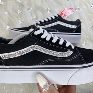 K&ouml;nnte beinhalten: Schwarze Vans-Sneaker aus Canvas mit einer wei&szlig;en Plateau-Sohle und einer Reihe von Strasssteinen auf dem seitlichen Streifen. Das Vans-Logo ist an der Seite des Schuhs sichtbar.