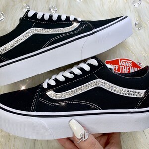 K&ouml;nnte beinhalten: Schwarze Vans-Sneaker aus Canvas mit wei&szlig;er Sohle und einer Reihe von Strasssteinen an der Seite. Das Vans-Logo ist an der Seite des Schuhs sichtbar.