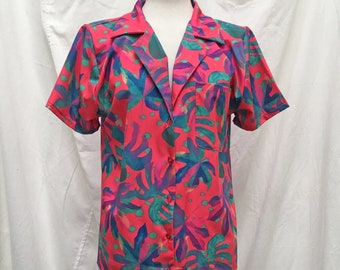 Peut inclure: Une chemise à manches courtes avec un motif de feuilles tropicales audacieux. La chemise présente un fond rouge vif, orné de grandes feuilles bleues, violettes et vertes. Elle a un col et une poche poitrine.