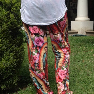 May include: Red, yellow, and blue printed pants with a religious image of a woman in a blue robe and a crown of flowers. The pants have a floral pattern with pink, white, and yellow flowers.