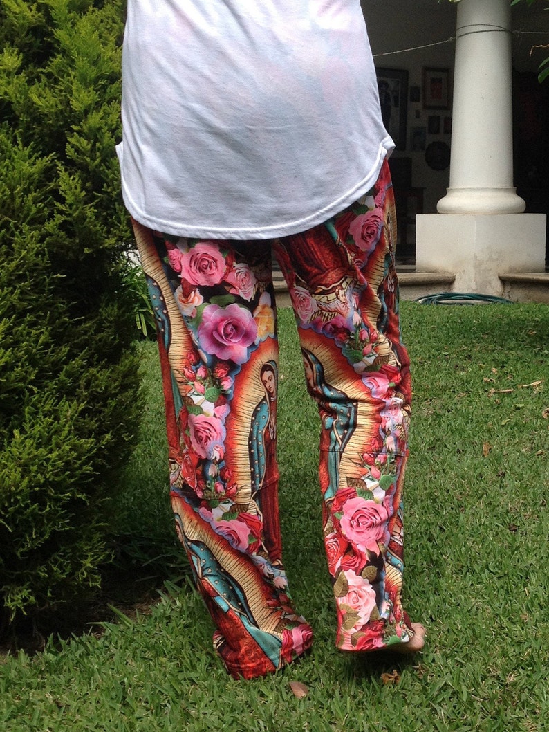May include: Red, yellow, and blue printed pants with a religious image of a woman in a blue robe and a crown of flowers. The pants have a floral pattern with pink, white, and yellow flowers.