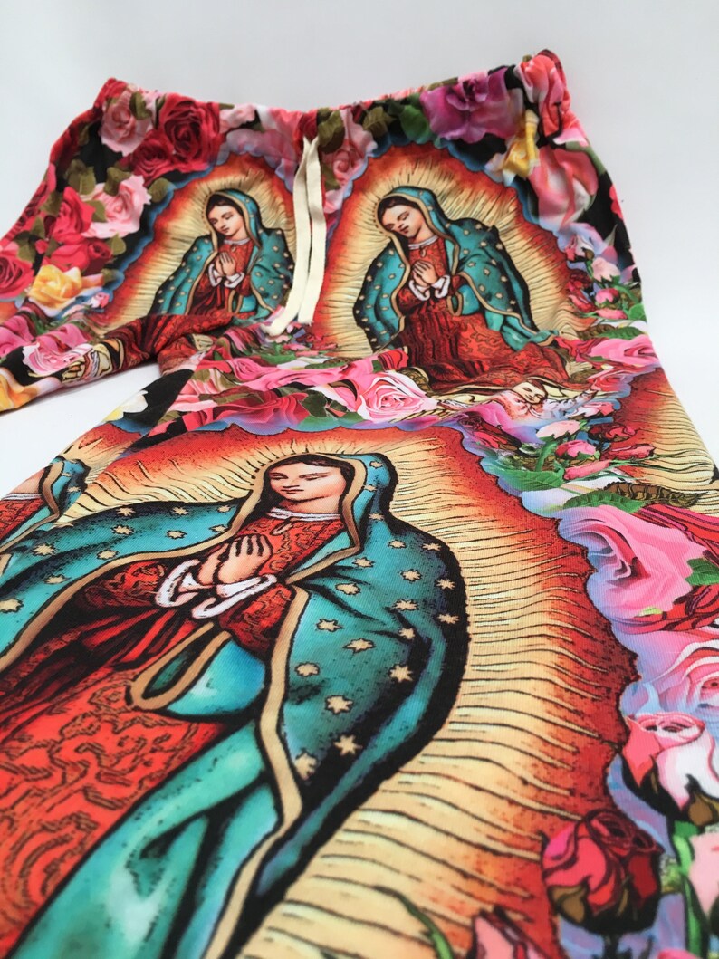 May include: A pair of colorful pants with a floral print featuring an image of the Virgin Mary. The pants have a drawstring waist and are made of a soft, comfortable fabric.