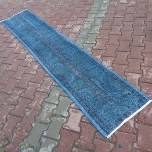 May include: A long, blue rug with a faded, intricate pattern. The rug is laid out on a brick patio.