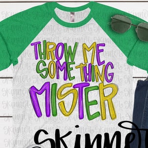 May include: A white long-sleeved shirt with a green and white raglan sleeve design. The shirt has the text "THROW ME SOMETHING MISTER" in purple, yellow, and green lettering. The text "Skinner doodles" is in black lettering below the other text.