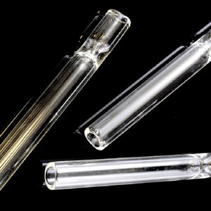 May include: Three clear glass smoking pipes of varying lengths. The pipes are made of smooth glass and have a rounded end.