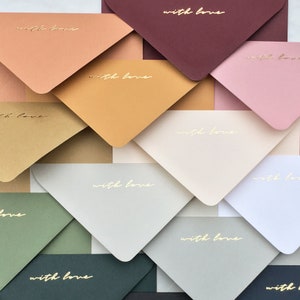 May include: A collection of colorful envelopes in various shades, including peach, gold, and green. Each envelope is printed with the words "with love" in gold script. The envelopes are arranged in a layered pattern.