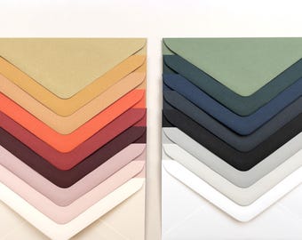 Pode incluir: Dois conjuntos de envelopes coloridos dispostos em forma de leque. Um conjunto apresenta tons quentes como bege, laranja e bordô. O outro conjunto mostra tons frios, incluindo tons de verde, azul e cinza. O envelope inferior de cada conjunto é branco.