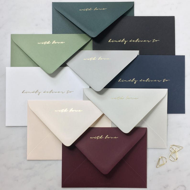 Pode incluir: Uma variedade de envelopes coloridos em v&aacute;rios tons, incluindo verde, preto e bord&ocirc;. Cada envelope apresenta texto dourado que diz "with love" ou "kindly deliver to". Os envelopes est&atilde;o dispostos sobre uma superf&iacute;cie branca.