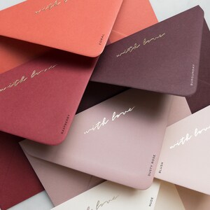 Pode incluir: Uma cole&ccedil;&atilde;o de envelopes coloridos em tons de coral, framboesa, bord&ocirc;, rosa empoeirado e nude. Cada envelope tem as palavras "with love" em escrita dourada. Os envelopes s&atilde;o rotulados com seus nomes de cores.