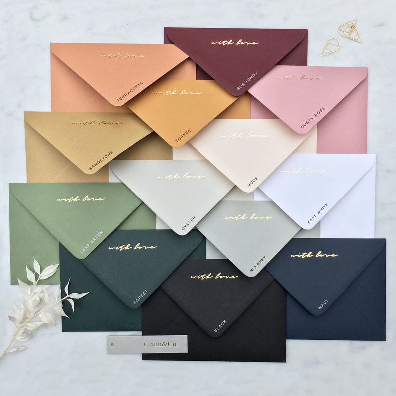 Pode incluir: Uma cole&ccedil;&atilde;o de envelopes coloridos em v&aacute;rias tonalidades, incluindo terracota, bord&ocirc; e azul marinho. Cada envelope &eacute; rotulado com um nome de cor e a frase "with love" em escrita dourada. Os envelopes est&atilde;o dispostos de forma atraente.