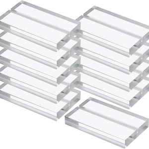 May include: Clear acrylic rectangular blocks, stacked in multiple groups. The blocks are transparent, allowing light to pass through. The edges are smooth and the overall appearance is clean and modern. Ideal for displaying signs or photos.