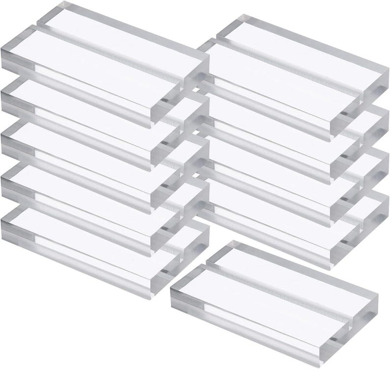 May include: Clear acrylic rectangular blocks, stacked in multiple groups. The blocks are transparent, allowing light to pass through. The edges are smooth and the overall appearance is clean and modern. Ideal for displaying signs or photos.