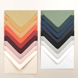 May include: Two stacks of colorful envelopes in various shades. The left stack features warm tones like beige, orange, and burgundy. The right stack showcases cool tones, including green, navy, and gray. Each envelope has a pointed flap.