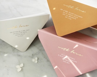 Pode incluir: Três envelopes triangulares nas cores branco, amarelo mostarda e rosa suave. Cada envelope apresenta o texto em dourado "with love" acima dos detalhes de endereço impressos para Mr. & Mrs. Elliot Galliardo, The Future Mr. & Mrs. Best e Alex Antonia.