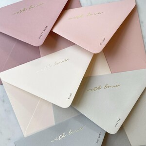 Pode incluir: Uma cole&ccedil;&atilde;o de envelopes em tons pastel, incluindo tons de rosa, bege e cinza. Cada envelope &eacute; impresso com as palavras "with love" em dourado. Os envelopes s&atilde;o rotulados com nomes de cores como "Dusty Rose" e "Blush".