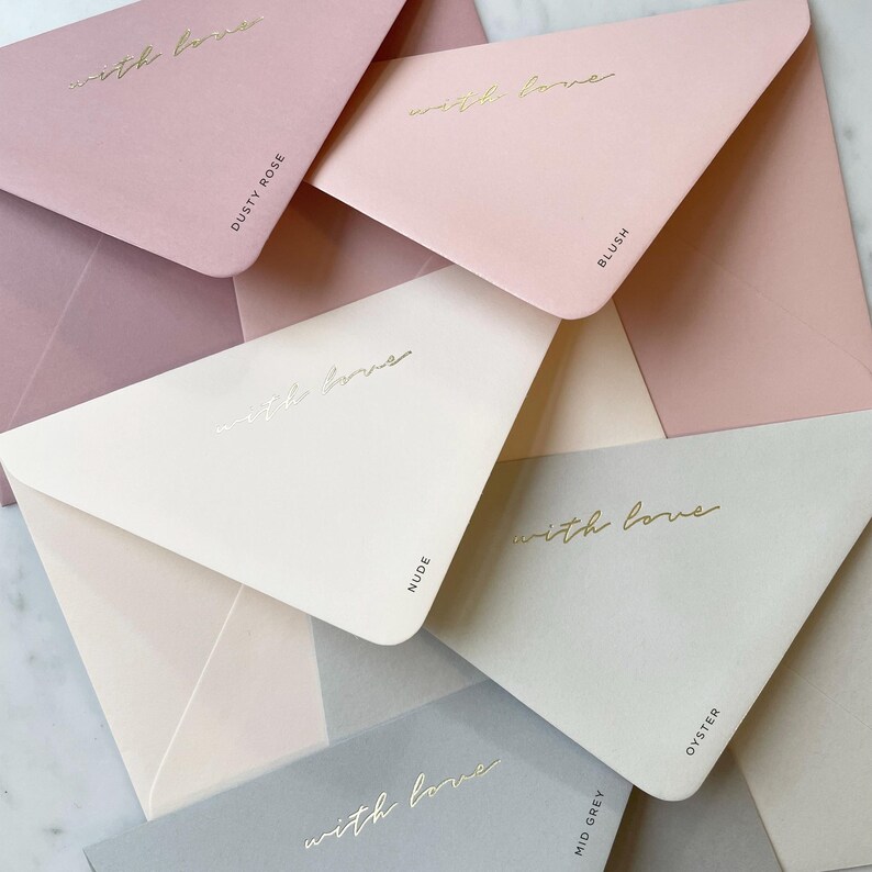 Pode incluir: Uma cole&ccedil;&atilde;o de envelopes em tons pastel, incluindo tons de rosa, bege e cinza. Cada envelope &eacute; impresso com as palavras "with love" em dourado. Os envelopes s&atilde;o rotulados com nomes de cores como "Dusty Rose" e "Blush".