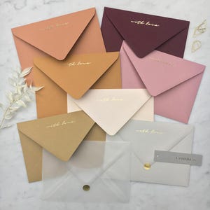 Pode incluir: Uma cole&ccedil;&atilde;o de envelopes coloridos, incluindo tons de rosa, castanho e bord&ocirc;, com a frase "with love" em escrita dourada. Alguns envelopes s&atilde;o transl&uacute;cidos. Uma etiqueta cinza diz "Crum & Co."