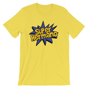 May include: A yellow t-shirt with the words "Super Hermano" in a blue and yellow comic book style design. The text is inside a blue starburst shape. The shirt is made of a soft material.