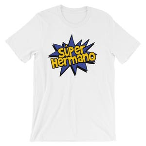 May include: White t-shirt featuring the text "Super Hermano" in yellow and black, set against a blue starburst design. The shirt is made of a soft material and has a crew neck.