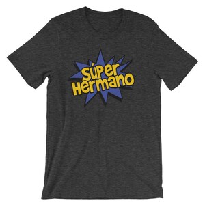 May include: Dark gray t-shirt with the text "S&uacute;per Hermano" in yellow, outlined in black, set against a blue starburst design. The shirt is a short-sleeved crew neck.