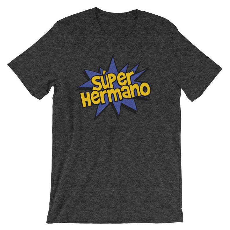 May include: Dark gray t-shirt with the text "S&uacute;per Hermano" in yellow, outlined in black, set against a blue starburst design. The shirt is a short-sleeved crew neck.