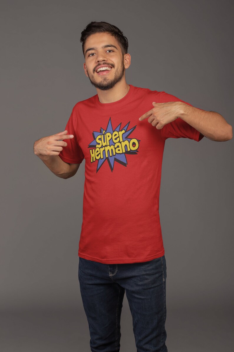 May include: Red t-shirt with the text "Super Hermano" in yellow and blue, a comic book style design. The shirt is paired with blue jeans.