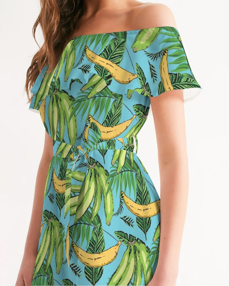 May include: A light blue off-the-shoulder dress with a tropical print featuring green leaves and yellow bananas.