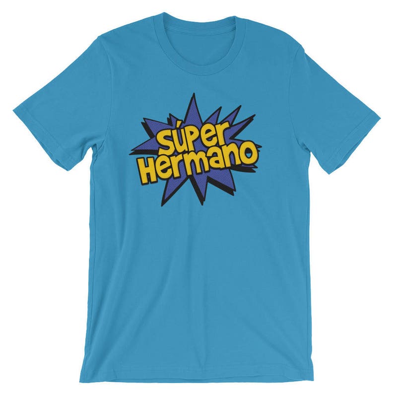 May include: A light blue t-shirt with the words "S&uacute;per Hermano" in yellow and black lettering inside a blue starburst design. The shirt is a crew neck style and appears to be made of a soft material.