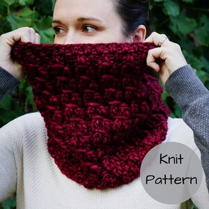 May include: A close-up of a burgundy knit cowl with a textured pattern. The cowl is held up by a person, obscuring their face. The text "Knit Pattern" is in a white circle.