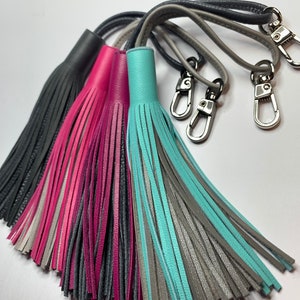 May include: Four leather keychains with tassels in gray, pink, teal, and gray. Each keychain has a silver swivel clasp.