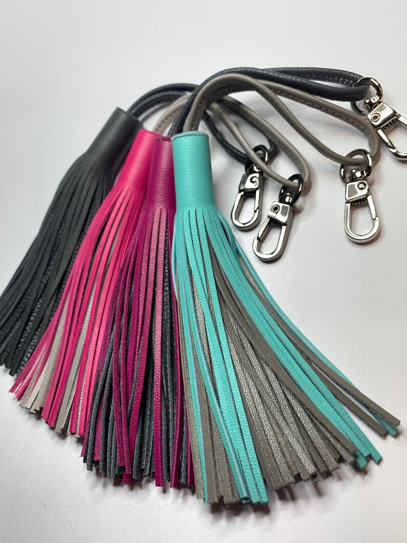 May include: Four leather keychains with tassels in gray, pink, teal, and gray. Each keychain has a silver swivel clasp.