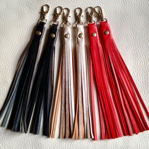 May include: Five leather tassel keychains with silver key rings. The tassels are in black, grey, beige, silver, and red.