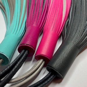 May include: Four leather tassels in turquoise, pink, black, and gray. The tassels are tied together with black, gray, and white cords.