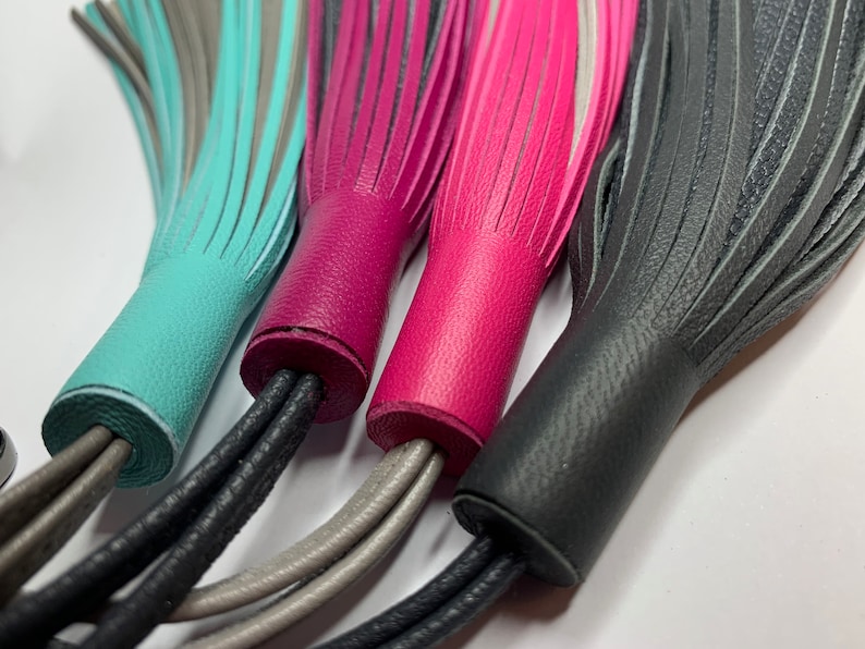 May include: Four leather tassels in turquoise, pink, black, and gray. The tassels are tied together with black, gray, and white cords.
