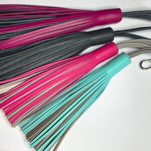 May include: Three leather tassels with different color combinations: pink and black, pink and gray, and teal and gray. The tassels are attached to cords with a silver key ring.