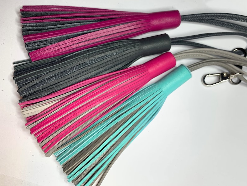 May include: Three leather tassels with different color combinations: pink and black, pink and gray, and teal and gray. The tassels are attached to cords with a silver key ring.