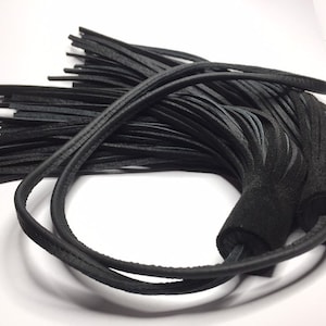 Puede incluir: Borla de cuero negro con flecos largos. La borla está unida a un lazo de cuero.