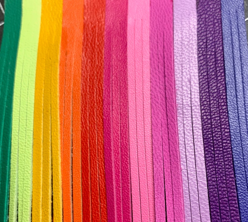 Op de afbeelding: Een regenboogassortiment van leren koorden, met een verscheidenheid aan kleuren, waaronder groen, geel, oranje, rood, roze, paars en blauw.