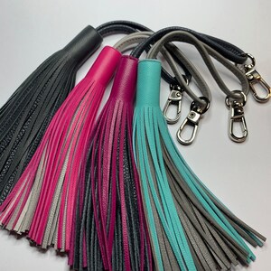 May include: Four leather tassels with different color combinations: black and gray, gray and pink, gray and magenta, and gray and turquoise. Each tassel has a silver metal loop.