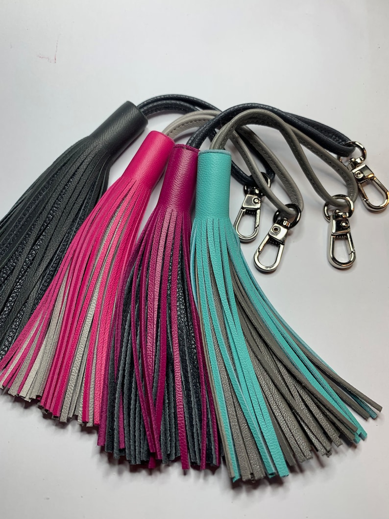 May include: Four leather tassels with different color combinations: black and gray, gray and pink, gray and magenta, and gray and turquoise. Each tassel has a silver metal loop.