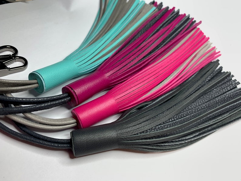 May include: Three leather tassels in turquoise, pink, and gray with black, gray, and white cords.