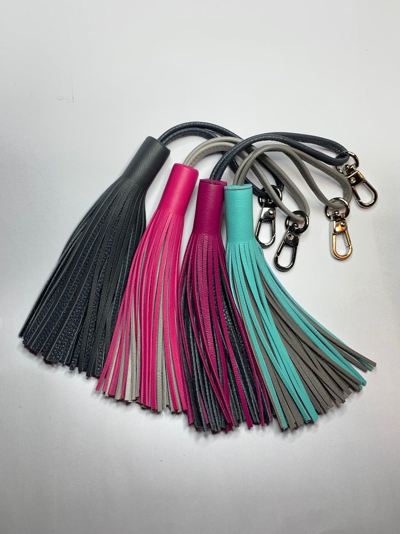 May include: Four leather tassels with keychains. The tassels are in shades of gray, pink, and teal.